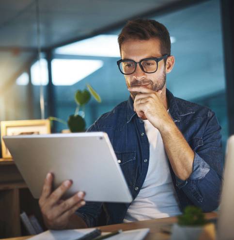 Shot of a young handsome businessman working late at night on his tablet in a modern office