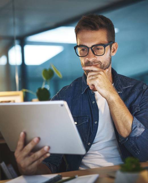 Shot of a young handsome businessman working late at night on his tablet in a modern office
